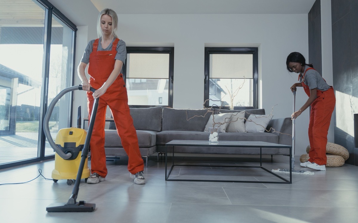 Two uniformed cleaners vacuuming and mopping a living room