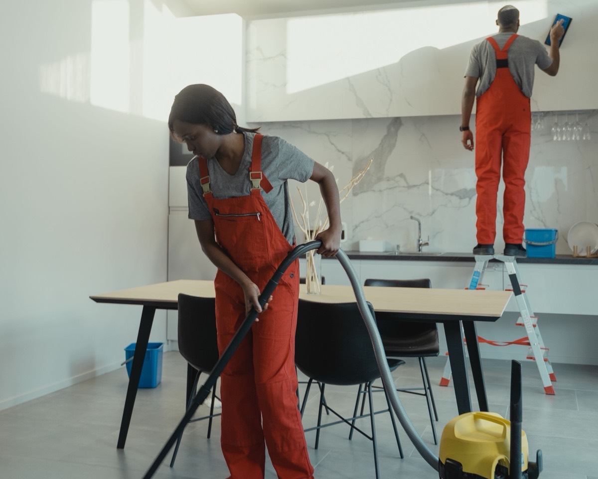 Cleaning team vacuuming a floor and detailing cabinets in a bright kitchen